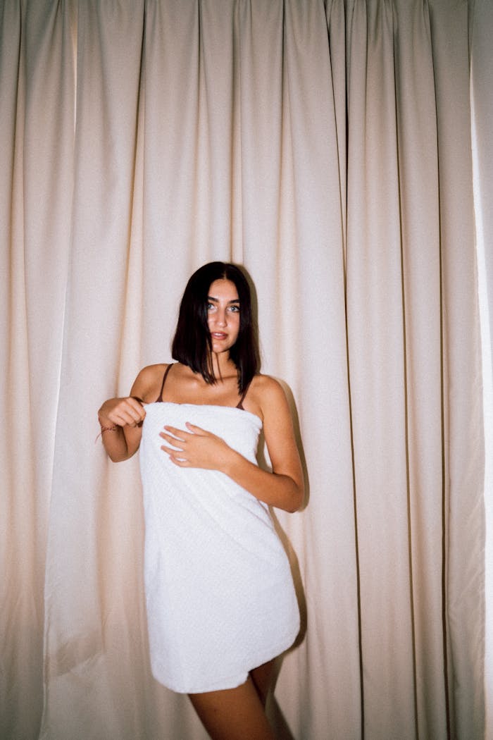 Portrait of a woman wrapped in a towel standing against curtain backdrop.