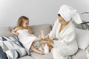 A mother and daughter enjoy bonding time on the sofa in cozy bathrobes, creating a warm family moment.