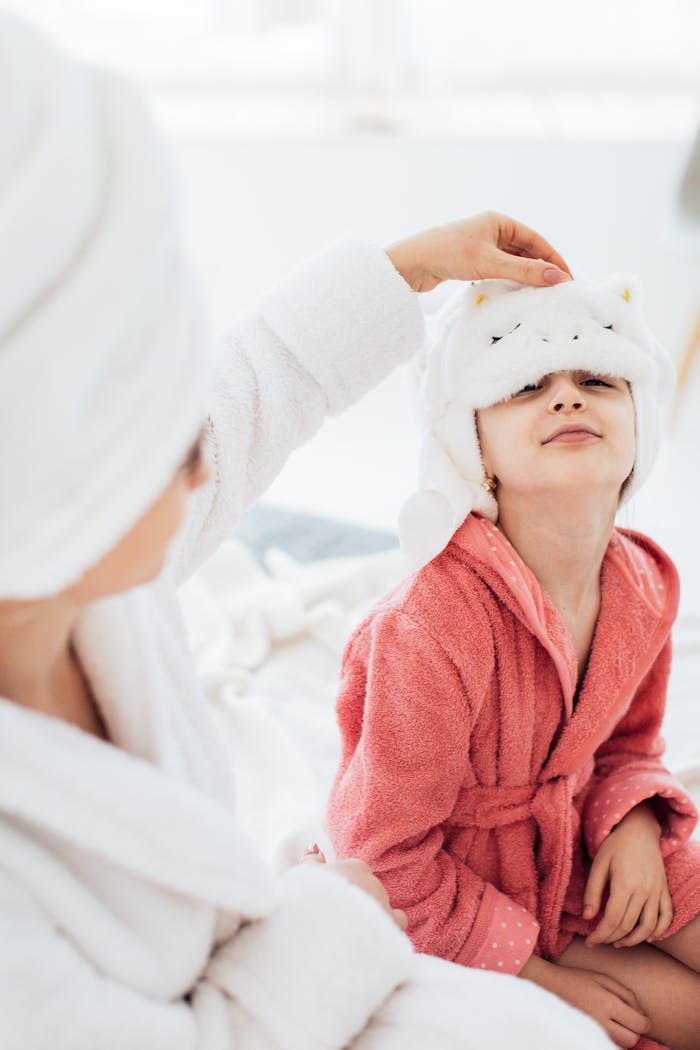 A mother and daughter in cozy bathrobes share a joyful moment in a bright bathroom setting.