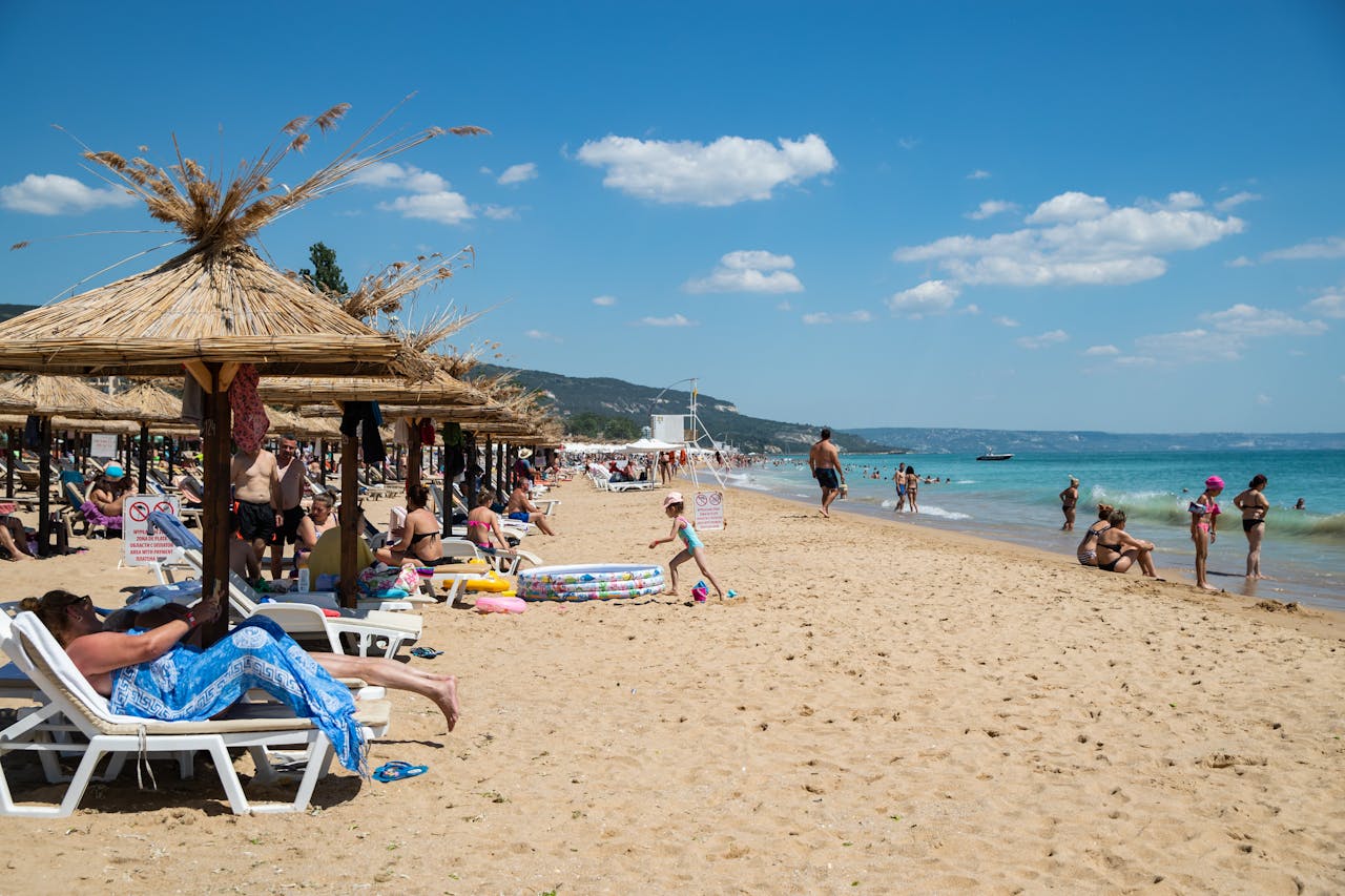 A lively beach scene with sunbathers, parasols, and vibrant activities under a clear sky.