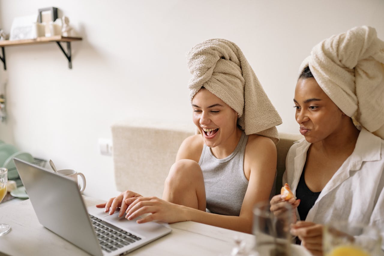 Two women laughing together with laptops, enjoying quality time indoors.